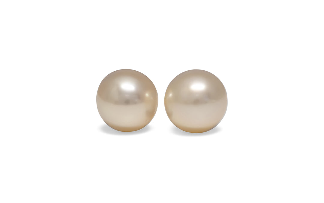 A pair of semi round, pink gold, golden south sea pearls are displayed on a white background.