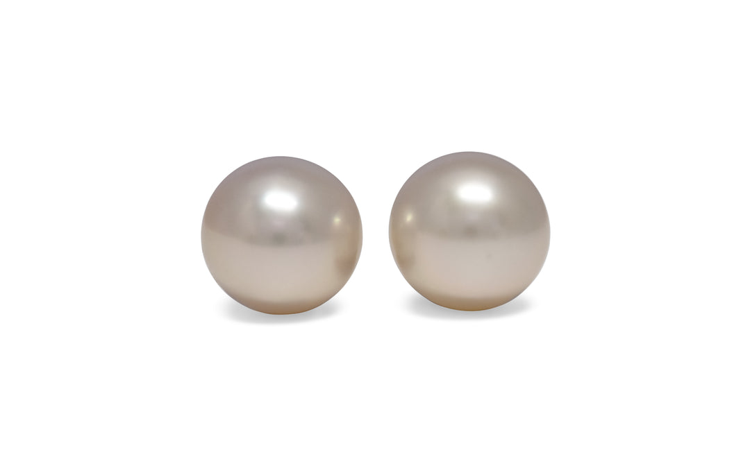 A pair of semi round, pink, white south sea pearls are displayed on a white background.