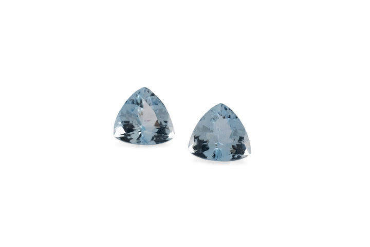A pair of trillion cut pale blue aquamarine gemstones are displayed on a white background.
