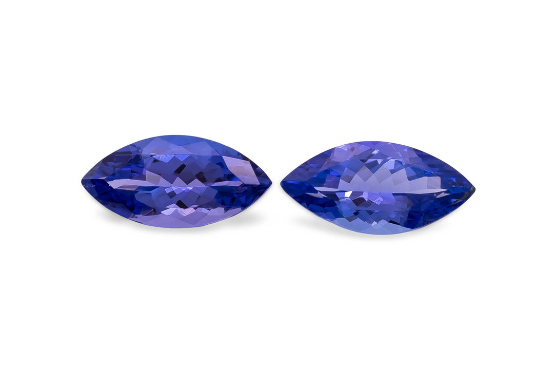 A pair of marquise cut purple blue tanzanite gemstones on a white background.