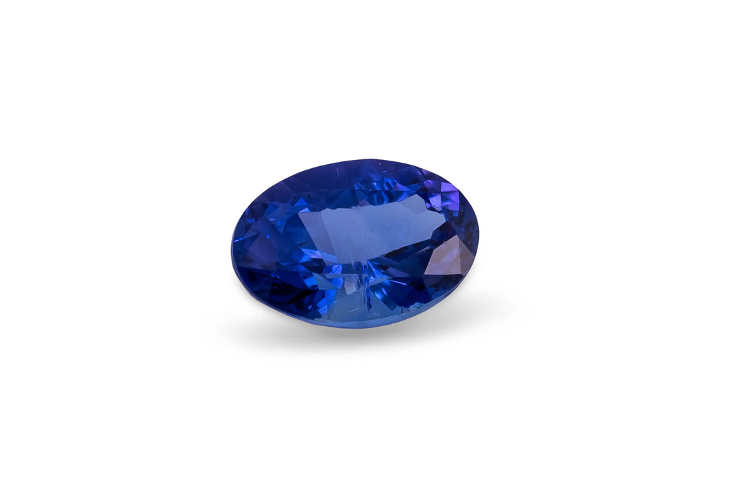Oval cut intense blue tanzanite gemstone on a white background.