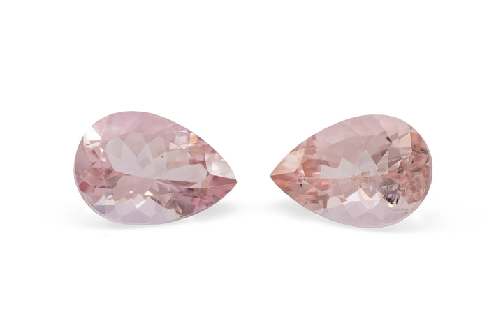 A pair of pear cut pale pink morganite gemstones on a white background.