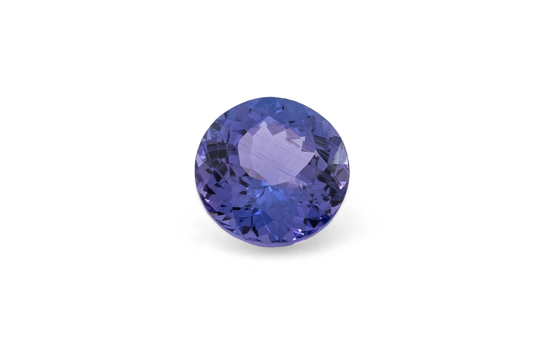 Round briliiant cut purple blue tanzanite gemstone on a white background.