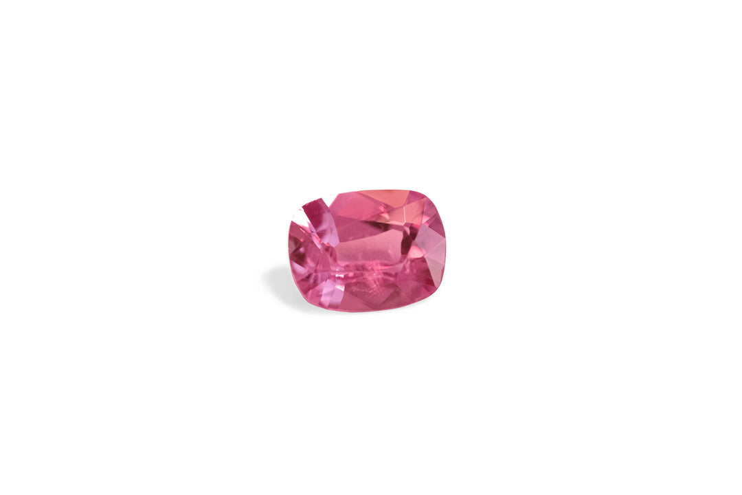 A cushion cut deep pink Ceylon sapphire gemstone is displayed on a white background.