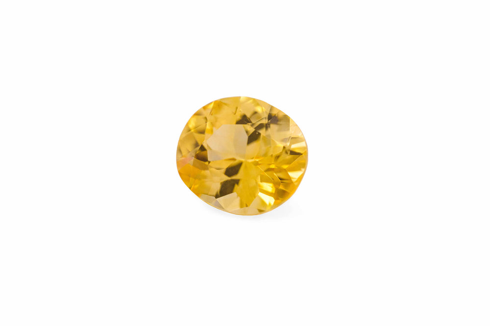 An oval cut golden yellow Ceylon sapphire gemstone is displayed on a white background.