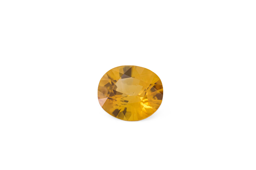 An oval cut rich golden yellow Ceylon sapphire gemstone displayed on a white background.