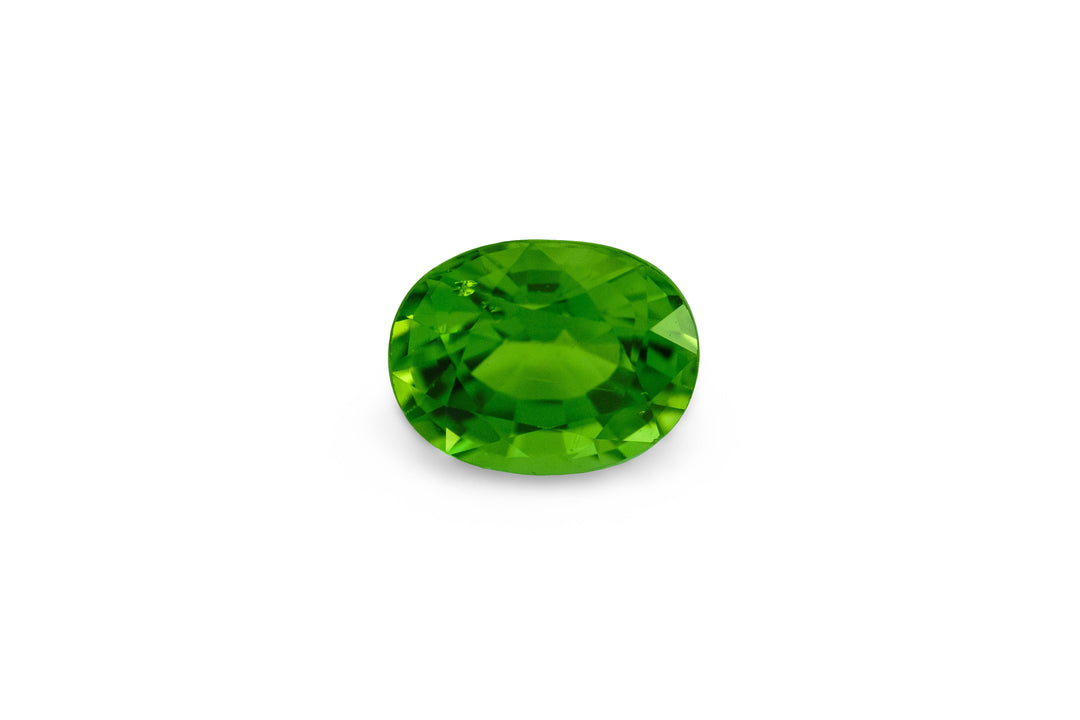 A cushion cut vibrant green tourmaline gemstone is displayed on a white background.