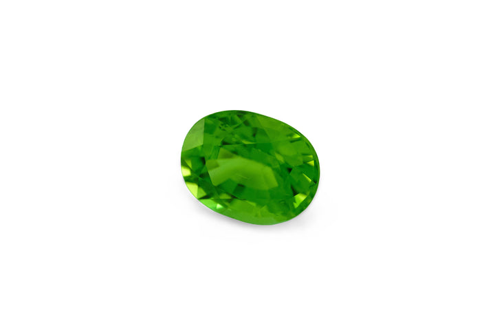 A cushion cut vibrant green tourmaline gemstone is displayed on a white background.