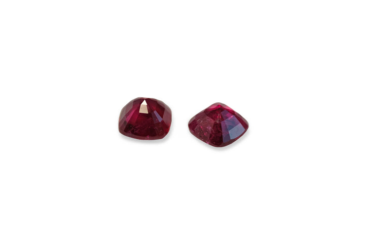 A pair of square cushion cut deep red ruby gemstones displayed on a white background.