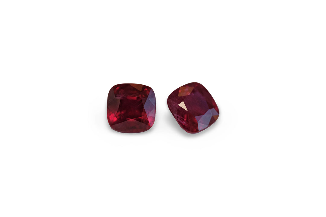 A pair of square cushion cut deep red ruby gemstones displayed on a white background.